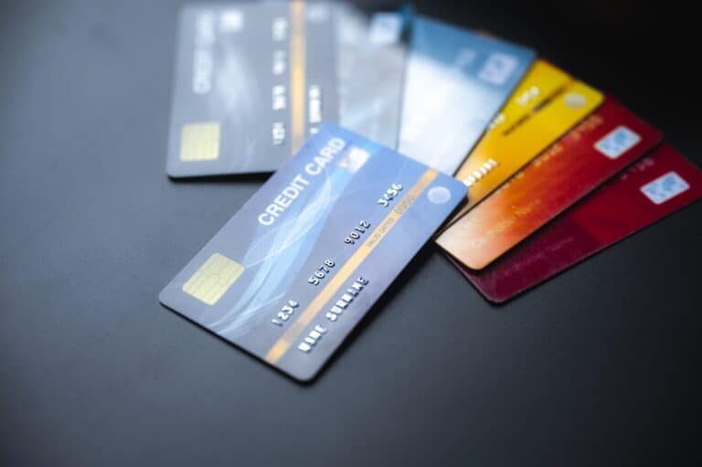 A close-up of five assorted credit and debit cards fanned out on a dark surface, with the closest card showing its chip and blurred numbers.